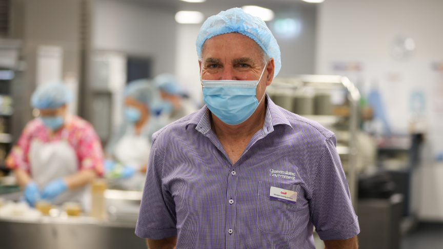 Photo of staff member Geoff Schultz in Toowoomba Hospital kitchen wearing face mask and hair cap