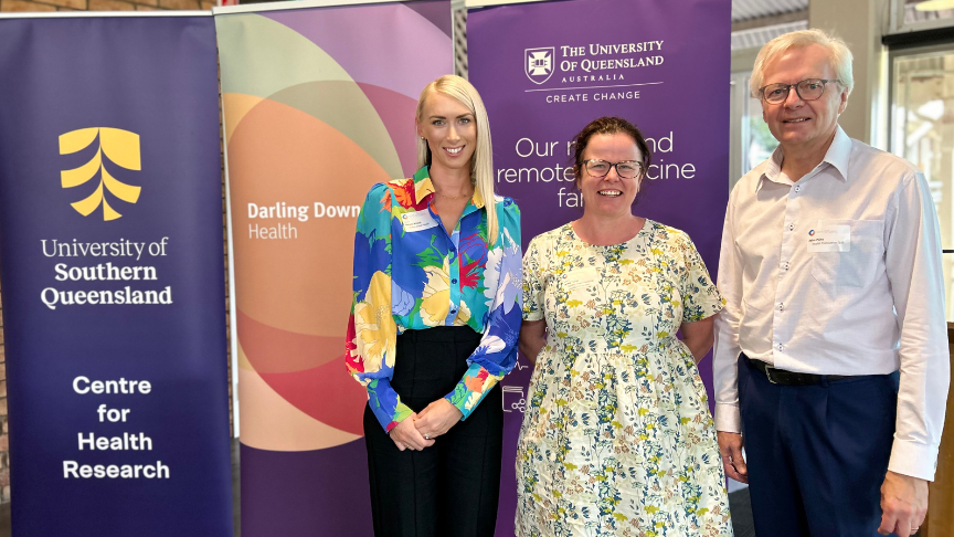 Three staff members standing in front of hospital and university stand up banners