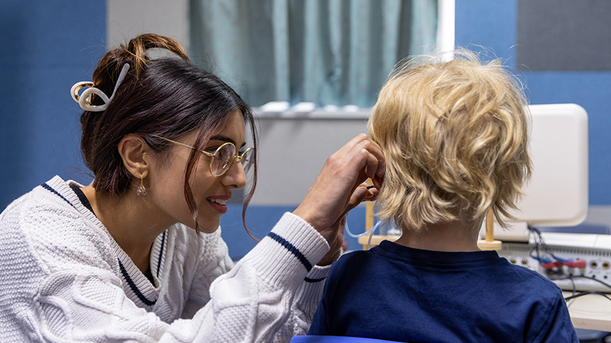 A female audiologist looking in a young boys ear.