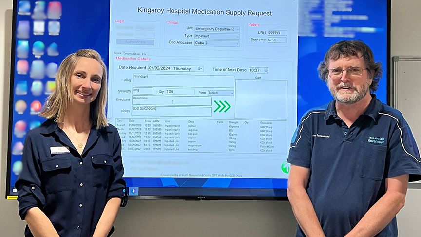 Kym Janes and Andrew Murray in front of a big screen displaying Kingaroy Hospital medication supply request form.