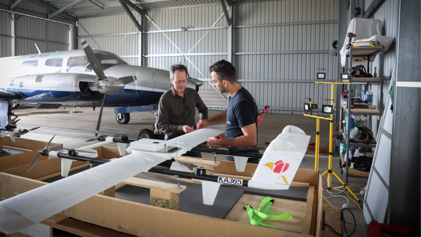 Paul Clayton and Daniel Scandar in an airplane hanger looking at an aircraft drone