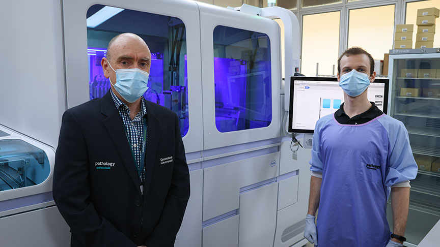 Two staff members wearing face masks in front of the new multiplex analyser.