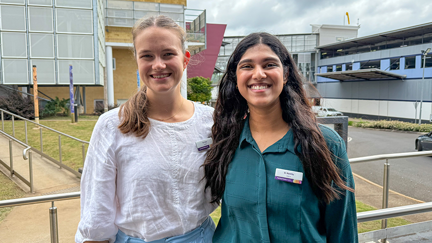 Two women stand side by side in front of a building, smiling and engaged in conversation.